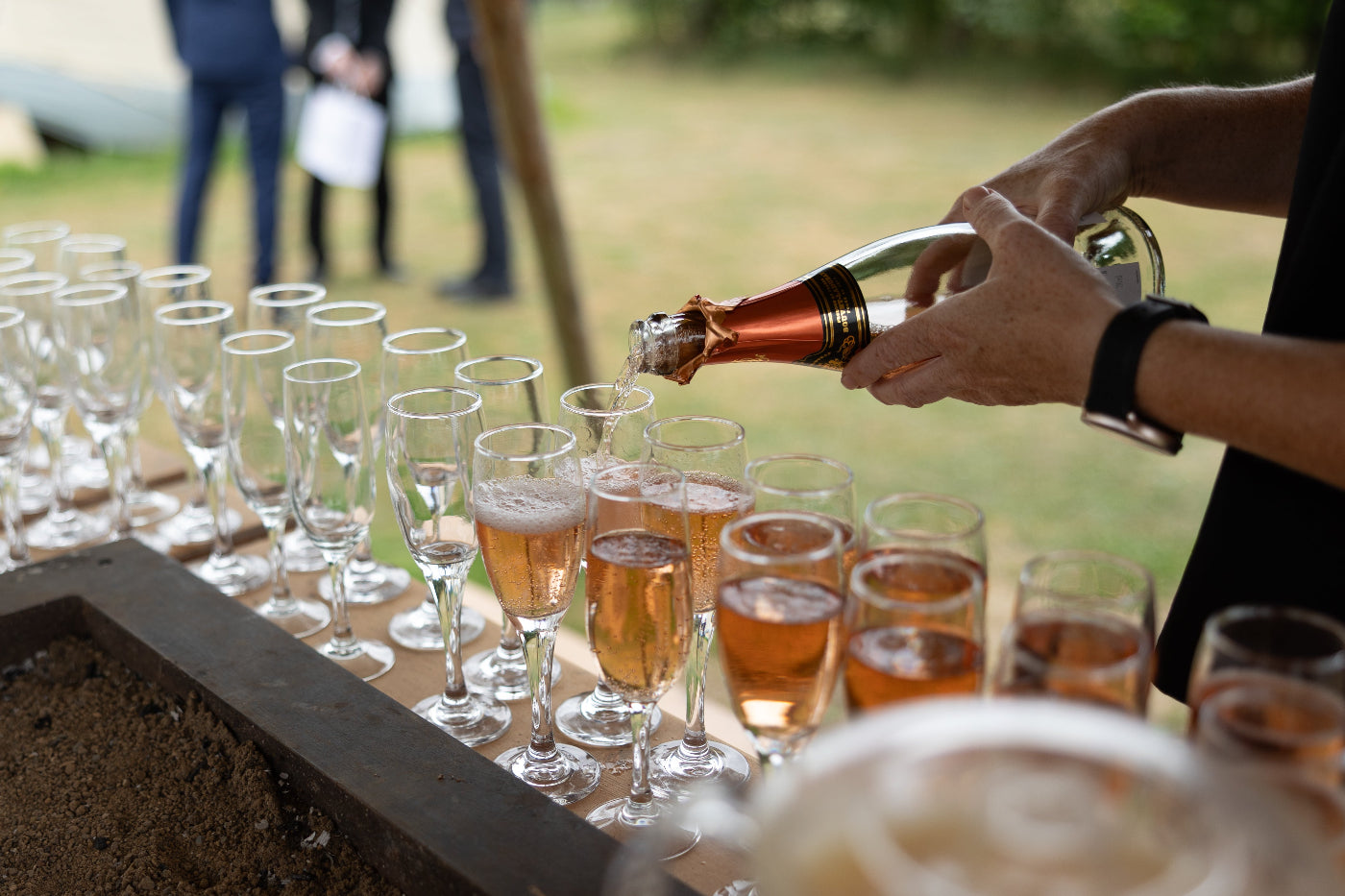 Person pouring champagne into glasses on a table outdoors