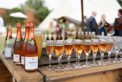 Bouvet champagne bottles and glasses on a wooden table outdoors with blurred people in the background