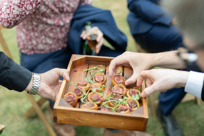 Wooden tray with small food items being passed between people outdoors